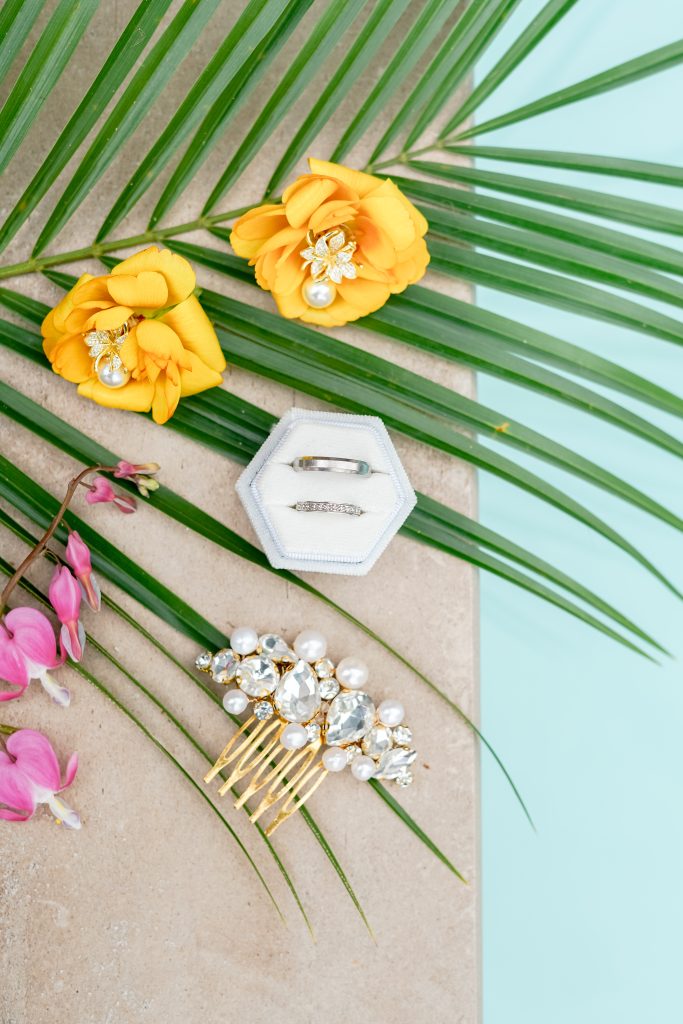 Détails élégants d’un mariage haut de gamme en Polynésie Flatlay de bijoux et de fleurs tropicales illustrant l’univers élégant et raffiné des mariages haut de gamme en Polynésie française organisés par Aroha Événements.