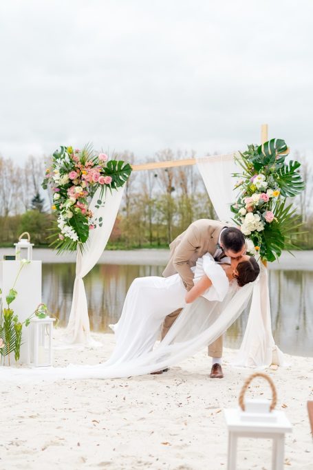 Un couple s'embrasse tendrement sous une arche florale près d'un lac.