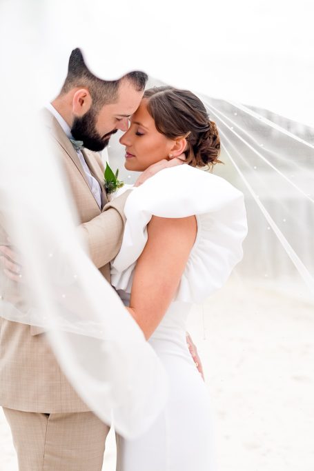 Un couple en tenue de mariage, se regardant tendrement sous un voile léger.