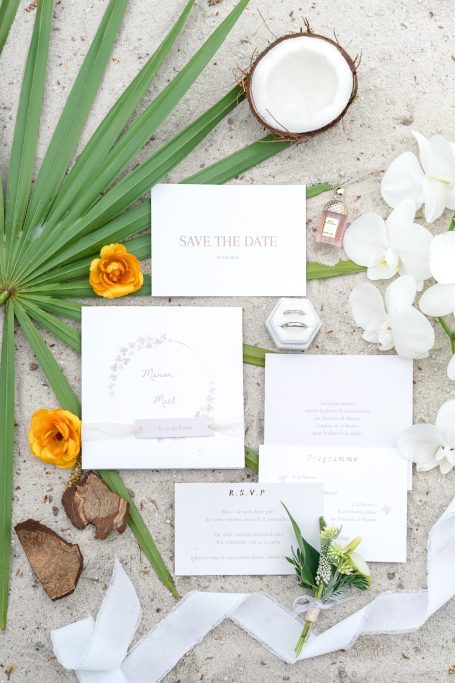 Composition d'invitations de mariage avec fleurs, feuilles, noix de coco et ruban.