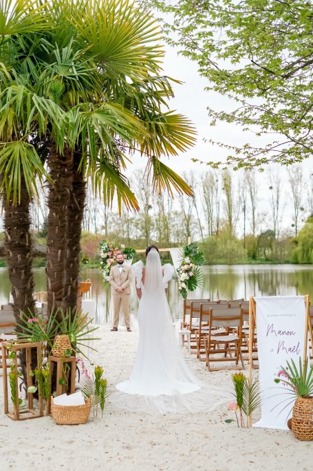 Cérémonie de mariage en extérieur, près d'un lac, avec des palmiers et des chaises en bois.