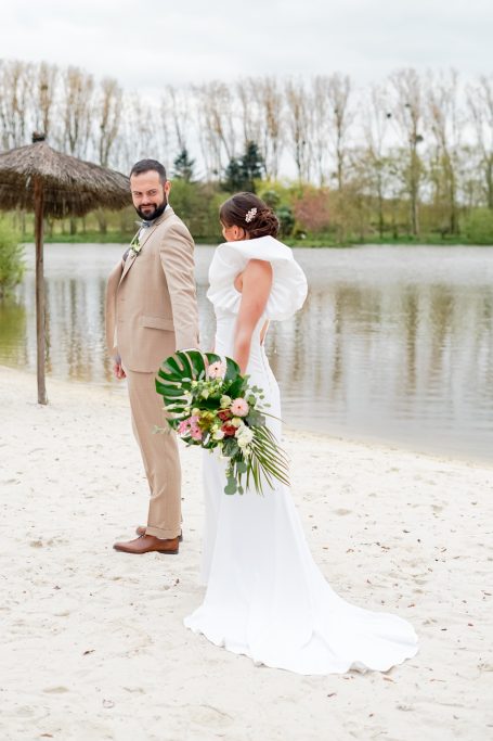 Mariée élégante en robe blanche, bouquet de fleurs, regardant son mari au bord de l'eau.