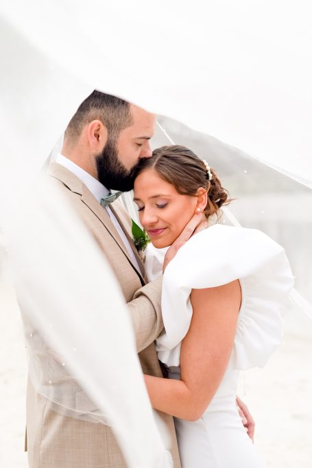 Un couple marié s'enlace tendrement sous un voile léger.