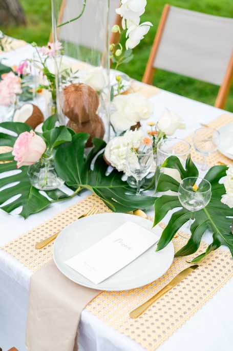 Décor de table élégante avec plantes, fleurs blanches et assiette sur nappe beige.