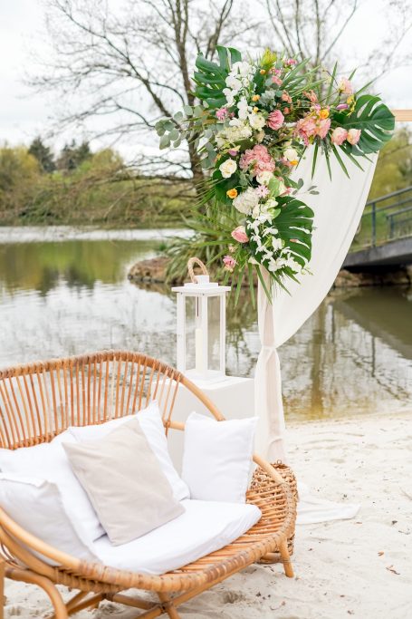 Décor floral romantique près d'un lac, avec un canapé en rotin et une lanterne.